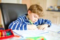 Portrait of frustrated crying sad school kid boy at home making homework. Little child writing with colorful pencils