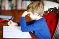 Portrait of frustrated crying sad school kid boy at home making homework. Little child writing with colorful pencils