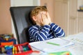 Portrait of frustrated crying sad school kid boy at home making homework. Little child writing with colorful pencils