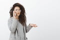 Portrait of frustrated questioned girlfriend with curly hair in grey coat and glasses, raising hand cluelessly while