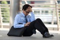 Portrait of frustrated stressed young Asian man sitting on the floor of sidewalk office and feeling tired with job