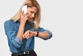Portrait of frustrated young blonde woman talking on mobile phone, looking at the watch, because her colleague is late Royalty Free Stock Photo
