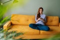Portrait of frustrated young woman sitting on couch at home using smartphone looking away pondering of problem. Anxious Royalty Free Stock Photo