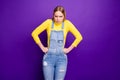 Portrait of frustrated youth put her hands on waist look wear yellow turtleneck denim jeans overalls isolated over Royalty Free Stock Photo