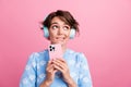 Portrait of funky charming minded girl hold smart phone biting lips look empty space isolated on pink color background