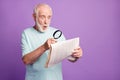 Portrait of funky shocked grey beard hair old man watching through magnifier newspaper isolated over purple background