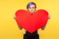 Portrait of funny amusing hipster girl holding big paper heart and sticking out rolled tongue. yellow background studio shot