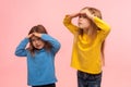 Portrait of funny amusing two little girls holding hands over eyes and looking far away with curious attentive expression Royalty Free Stock Photo