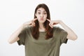 Portrait of funny attractive female student in dark t-shirt, holding breath in mouth and holding index fingers on cheeks