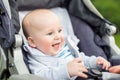 Portrait of funny baby boy laughing outdoors. Cute adorable child having fun sitting in stroller during walk Royalty Free Stock Photo