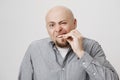 Portrait of funny bald caucasian man touching his tooth as if wanting to pull it out, standing with concentrated