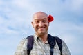 Portrait of a funny bald man against the sky with a red flower at the head