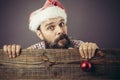 Portrait of a funny bearded man with santa cap holding a red round Christmas ball Royalty Free Stock Photo