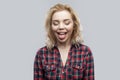 Portrait of funny beautiful blonde young woman in casual red checkered shirt standing with closed eyes and tongue out Royalty Free Stock Photo