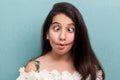 Portrait of funny beautiful brunette young girl with black long straight hair in white dress standing with crossed eyes, fish lips