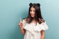 Portrait of funny beautiful brunette young girl with black long straight hair in white dress standing, looking away with finger up Royalty Free Stock Photo