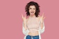 Portrait of funny beautiful brunette young woman with curly hairstyle in casual style standing with rock sign and looking at