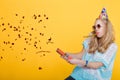 Portrait of funny blond woman in birthday hat and red confetti on yellow background. Celebration and party. Royalty Free Stock Photo