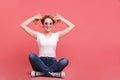 Portrait of funny blond woman 20s wearing vintage sunglasses laughing while sitting on floor with legs crossed Royalty Free Stock Photo