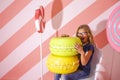 Portrait of Funny Caucasian Teenager Girl Biting Huge Artistic Colorful Macarons Against Striped Background