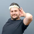 Portrait of funny chubby man wearing flower wreath on head and behaving feminine against gray background
