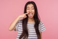 Portrait of funny comical girl with long hair in striped t-shirt picking nose, pulling boogers and showing tongue Royalty Free Stock Photo