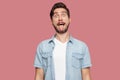 Portrait of funny crazy handsome bearded young man in blue casual style shirt standing with big eyes, tongue out and looking at Royalty Free Stock Photo