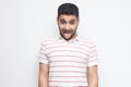 Portrait of funny crazy handsome bearded young man in striped t-shirt standing, tongue out and looking at camera with funny face Royalty Free Stock Photo