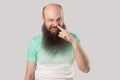 Portrait of funny dirty middle aged bald man with long beard in light green t-shirt standing drilling with finger on his nose,