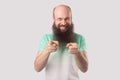 Portrait of funny excited middle aged bald man with long beard, green t-shirt standing, pointing and looking at camera with toothy