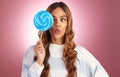 Portrait, funny face and lollipop with a woman on a pink background in studio holding giant candy. Comic, comedy and