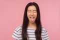 Portrait of funny girl with long hair in striped t-shirt showing tongue and keeping eyes closed with naughty childish grimace