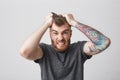 Portrait of funny good-looking bearded caucasian man with tattoo on left arm and stylish hairstyle holding hair with Royalty Free Stock Photo