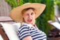 Portrait of funny grimace childish young adult woman in hat and dress sitting and resting on cozy sunbed, winking and showing Royalty Free Stock Photo