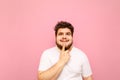 Portrait of a funny happy fat man in white t-shirt on a pink background, looks up at copy space with a smile on his face. A happy