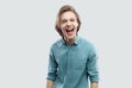 Portrait of funny happy handsome long haired blonde young man in blue casual shirt standing, laughing and looking at camera Royalty Free Stock Photo