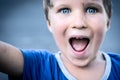 Portrait of a funny happy mischievous cheerful cute blond blue eyed boy making freckles dirty face while playing