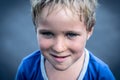 Portrait of a funny happy mischievous cheerful cute blond blue eyed boy making freckles dirty face while playing