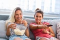 Portrait of funny and happy young women watching comedy in bed and laughing. Cheerful friends eating tasty popcorn and looking Royalty Free Stock Photo