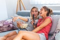 Portrait of funny and happy young women watching comedy in bed and laughing. Cheerful friends eating tasty popcorn and looking Royalty Free Stock Photo