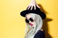 Portrait of funny hipster girl, touching her hat with hand, wearing sunglasses, isolated on yellow background. Royalty Free Stock Photo