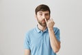 Portrait of funny impolite caucasian man with beard, picking nose with pinky staring with lifted eyebrow at camera Royalty Free Stock Photo