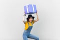 Funny joyful woman in blue denim overalls holding big present box above her head, looking at camera. Royalty Free Stock Photo