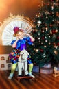 Portrait of funny laughing 4 years old girl in carnival venetian mask on rocking horse. Christmas tree, big clock on background. Royalty Free Stock Photo