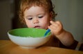 Portrait of funny little baby boy eating from plate holding spoon closeup. Royalty Free Stock Photo