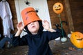 Portrait of funny little kid in wizard costume near door of house, putting candy bucket for trick or treat on head and saing boo.