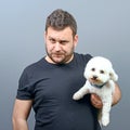 Portrait of funny looking chubby man holding cute small Bichon Frise puppy against gray background