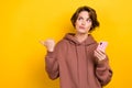 Portrait of funny minded ponder girl wear brown sportswear look directing empty space hold smartphone isolated on yellow Royalty Free Stock Photo