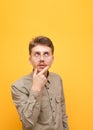 Portrait of funny nerd student on yellow background, wears glasses and beige shirt, looks up at copy space and thinks. Guy geek