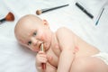 Portrait of a funny newborn baby with red lipstick kisses on the skin with scattered makeup tools on white background. top view Royalty Free Stock Photo